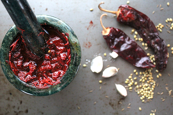 homemade harissa paste in mortar and pestle next to dried chiles