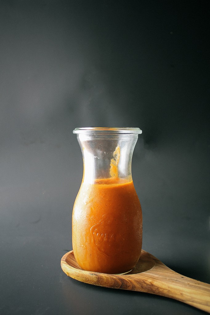 homemade red enchilada sauce in glass pitcher resting on wood spoon