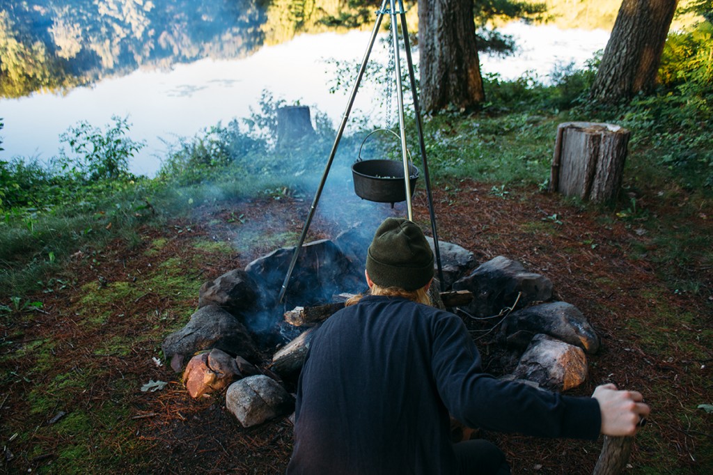 man stoking campfire with pot of three bean chili suspended over it