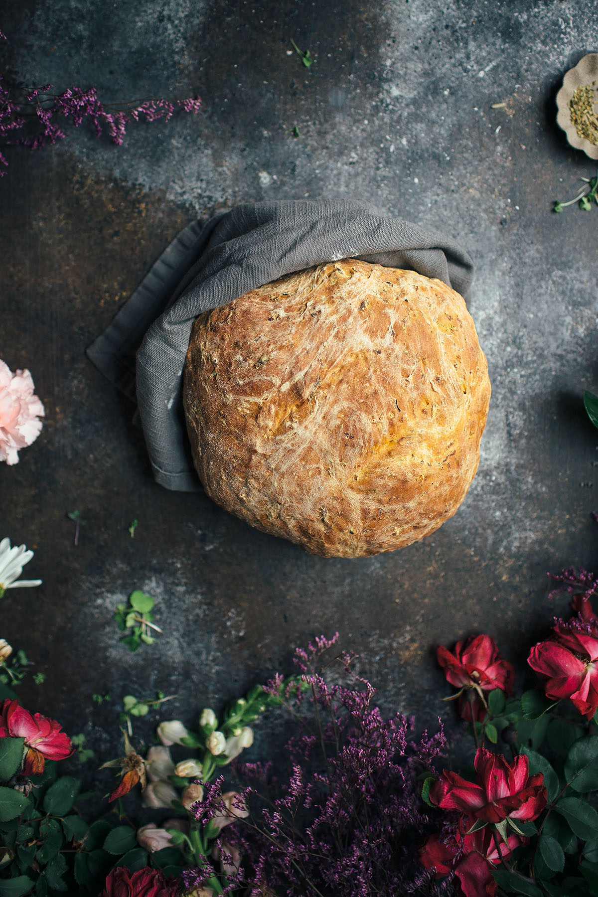 loaf of vegetable bread wrapped in a gray towel next to flowers