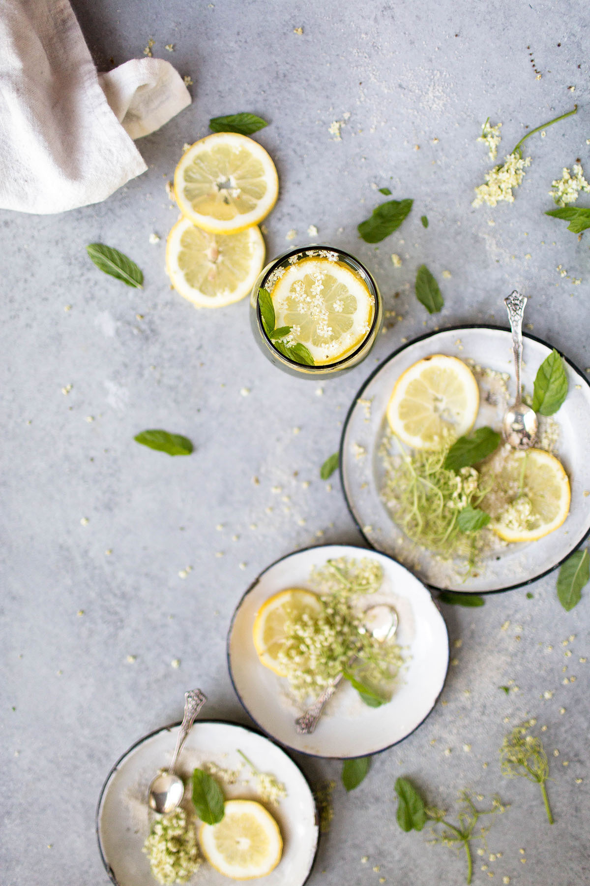 glass of elderflower lemonade surrounded by fresh elderflower blossoms and lemon slices