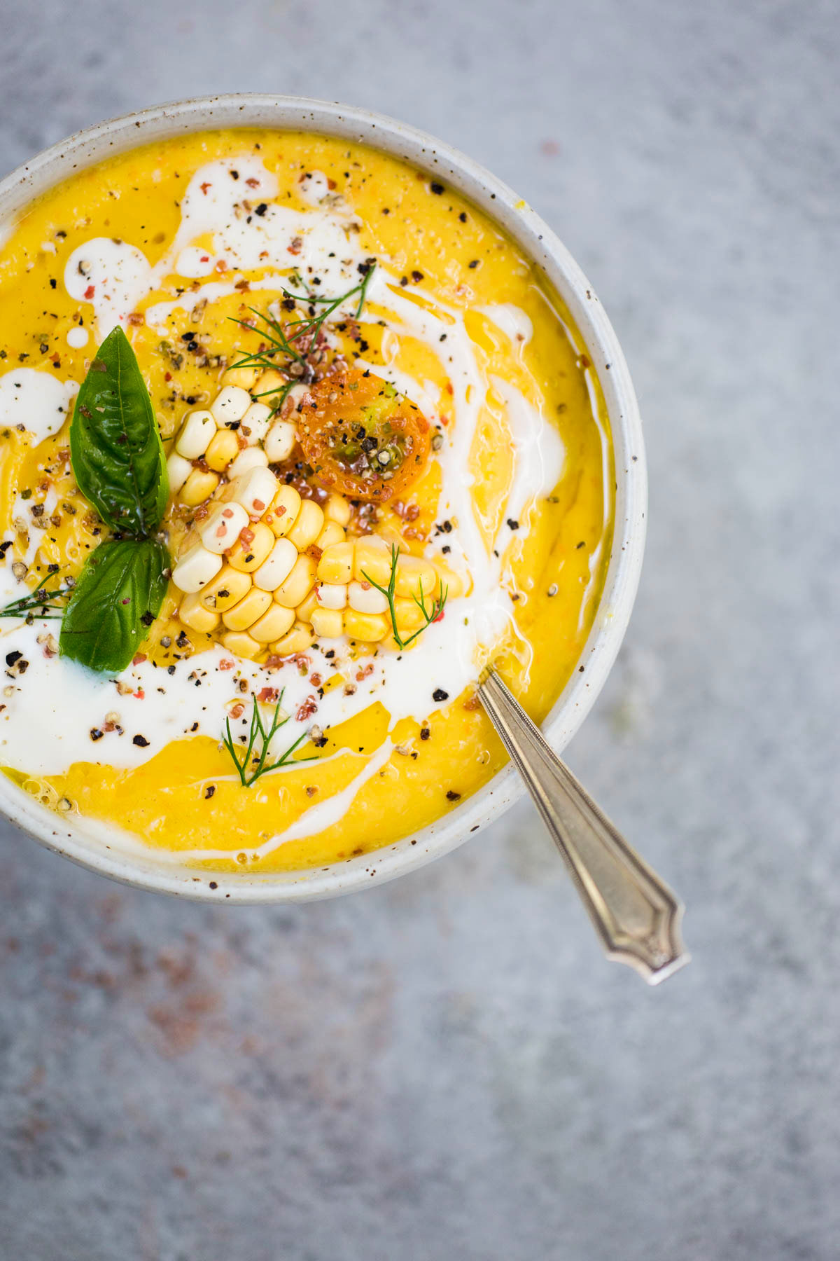 close up of sweet corn and tomato gazpacho garnished with raw corn, basil, and black pepper