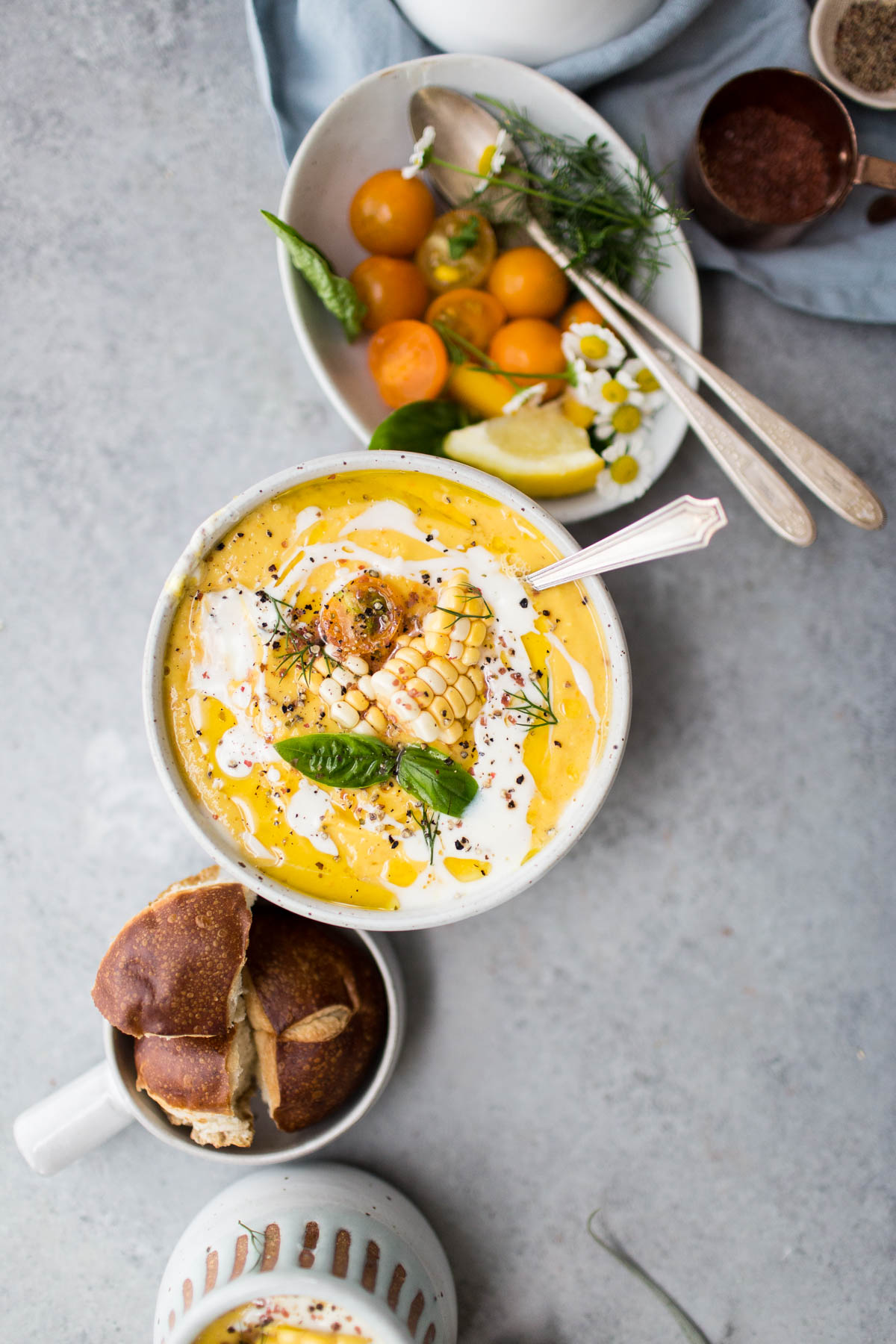 sweet corn and tomato gazpacho in white bowl beside bowl of ingredients 