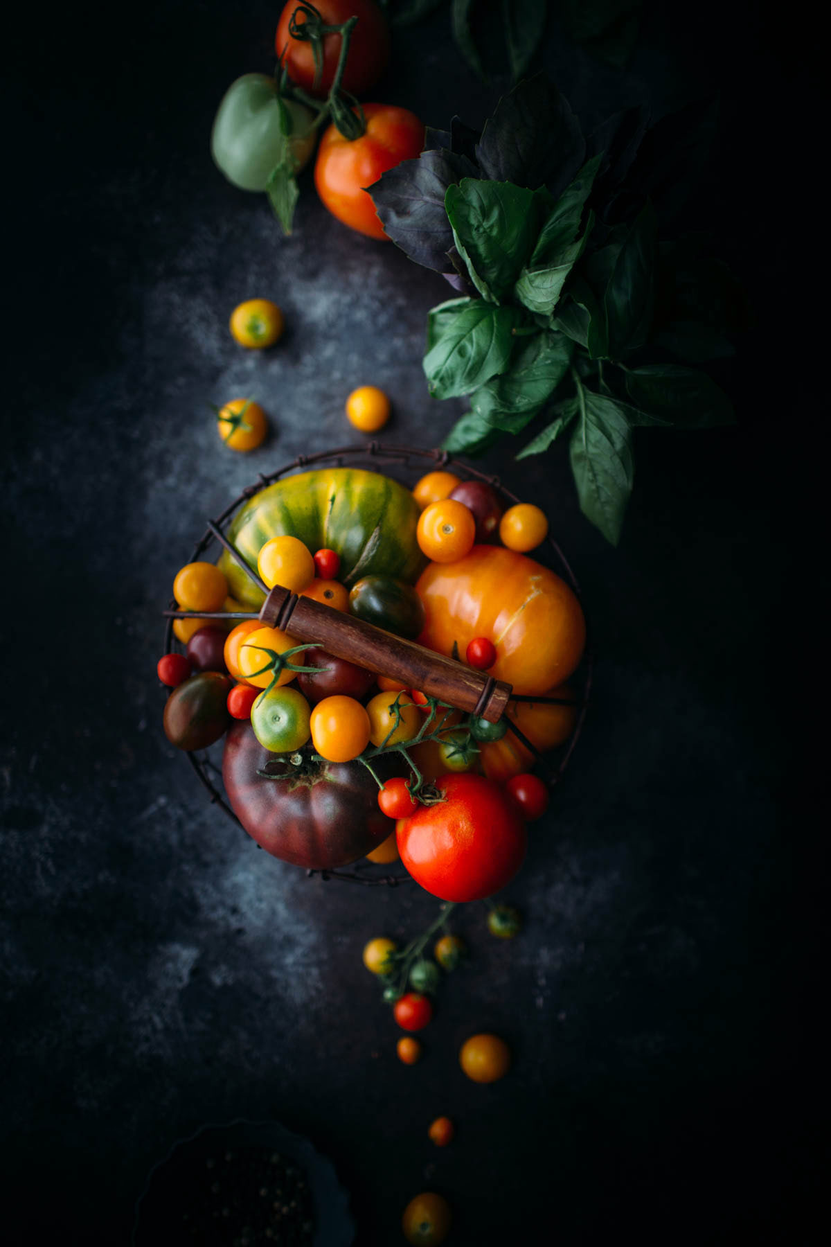 heirloom tomatoes in wire basket next to bunch of basil