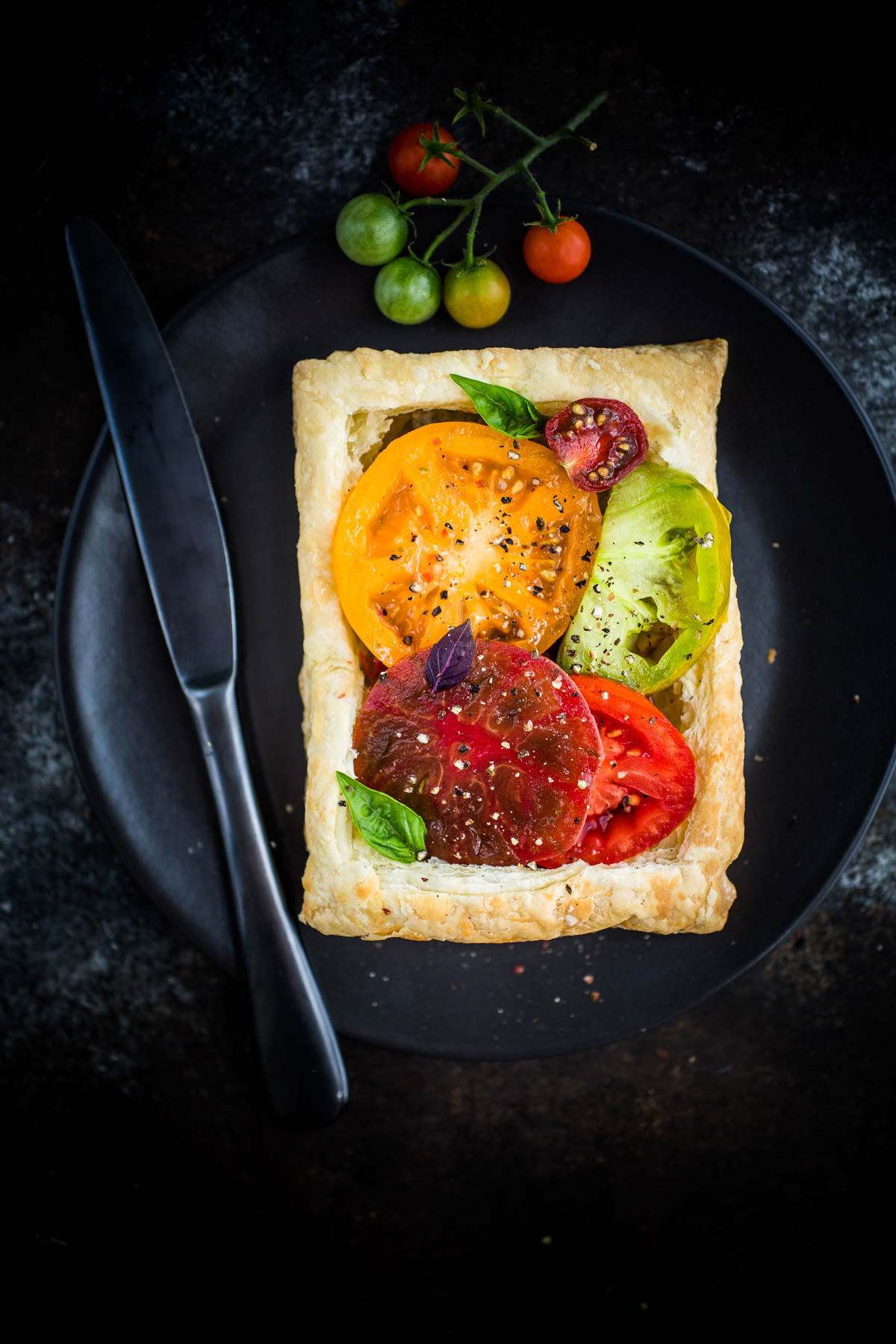 puff pastry tomato tart on dark plate with knife 