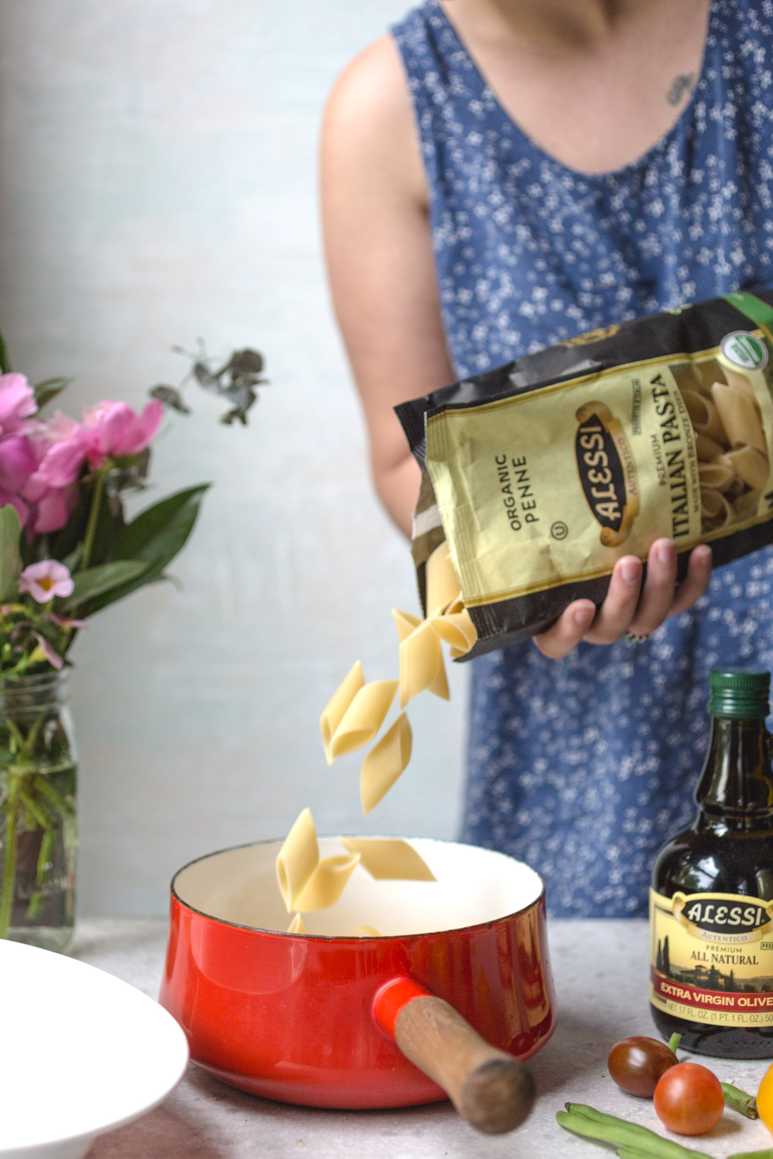 adding penne pasta to a red saucepan 