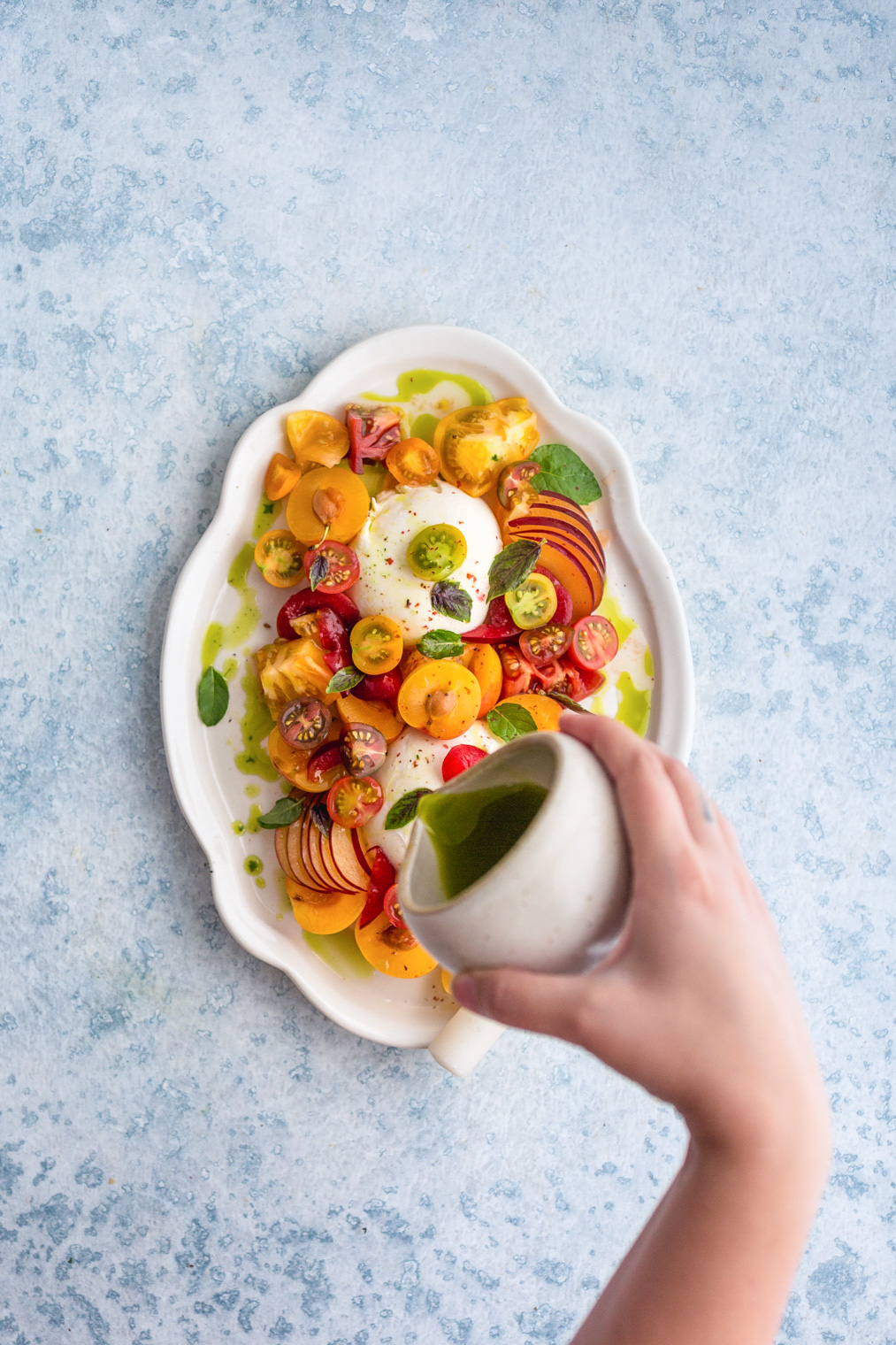 pouring basil oil over top of burrata tomato salad