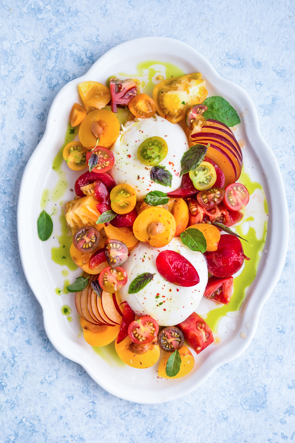 Burrata caprese with Plums Tomatoes and Mint-Basil Oil on white serving platter