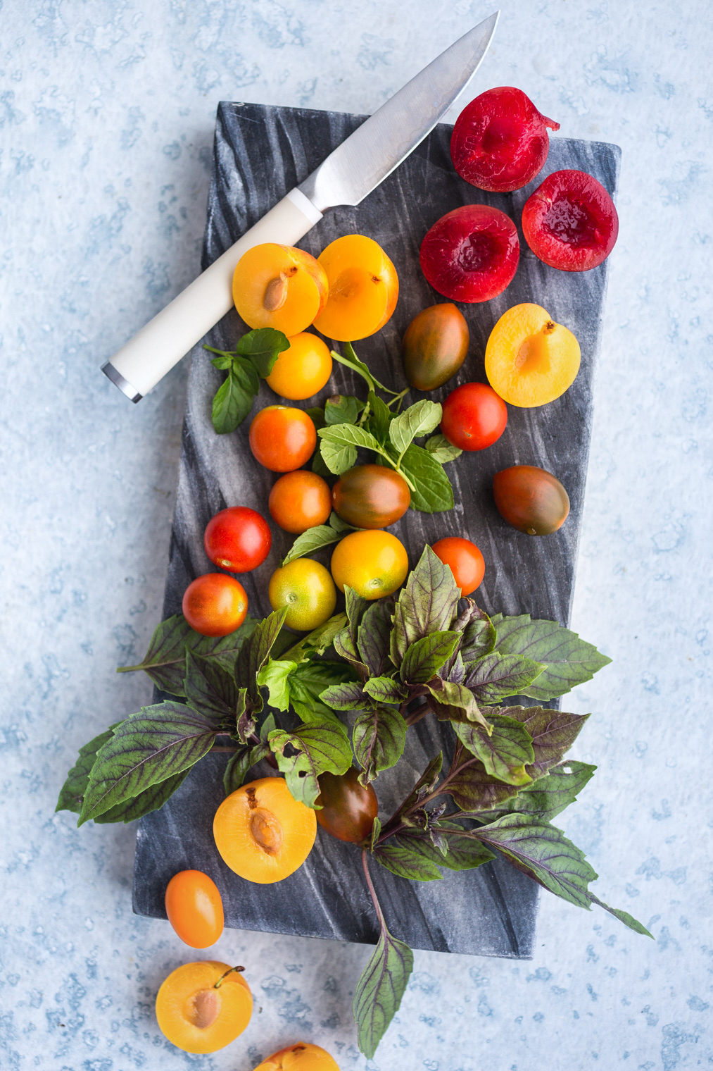 fresh plums, tomatoes, and herbs on gray serving board