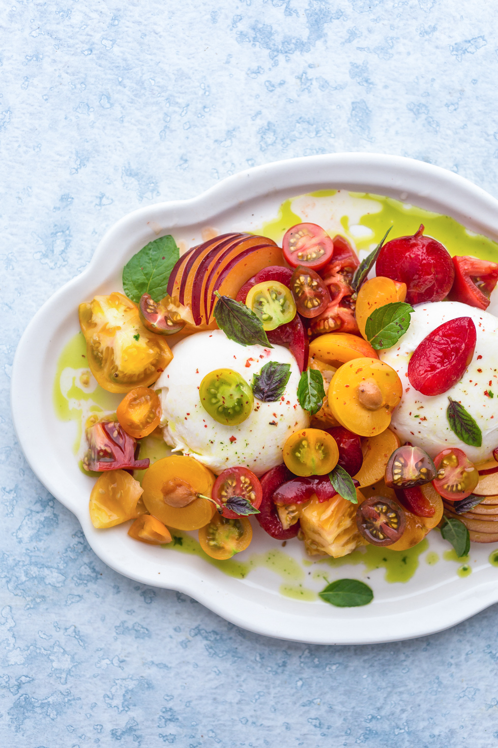 Burrata caprese with Plums Tomatoes and Mint-Basil Oil on white serving platter