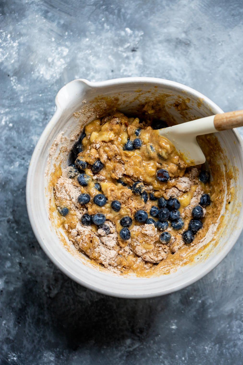 blueberry banana bread batter in white mixing bowl with rubber spatula