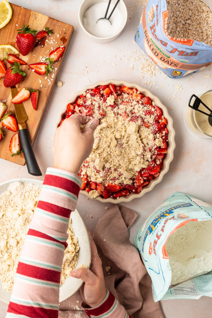 sprinkling the topping onto a gluten free strawberry rhubarb crisp
