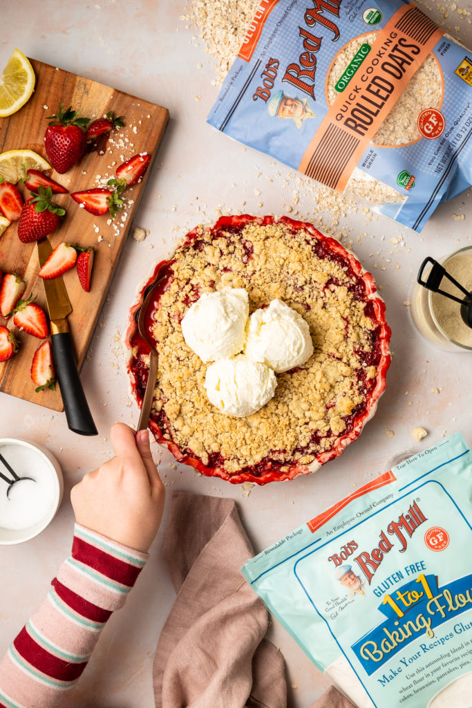 preparing to serve a rhubarb and strawberry crisp that's topped with scoops of vanilla ice cream