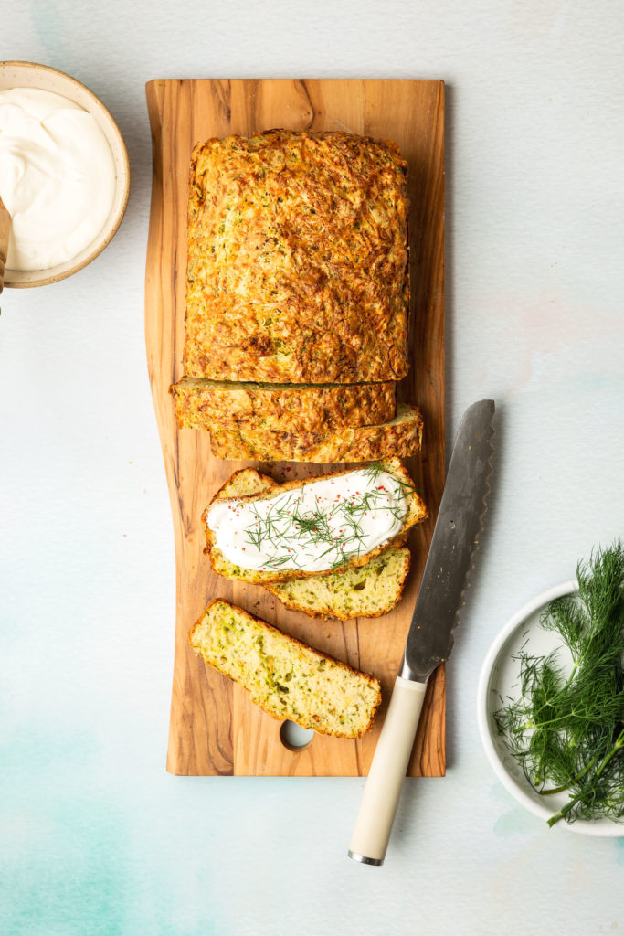 partially sliced loaf of Zucchini cheese Bread on wood cutting board