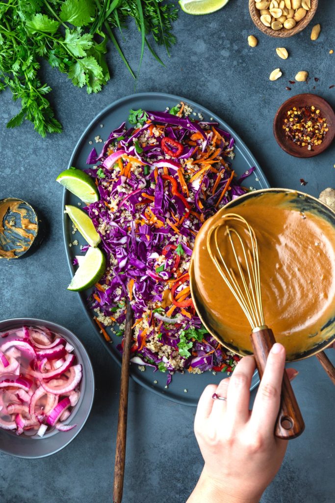 pouring peanut ginger dressing over a thai quinoa salad