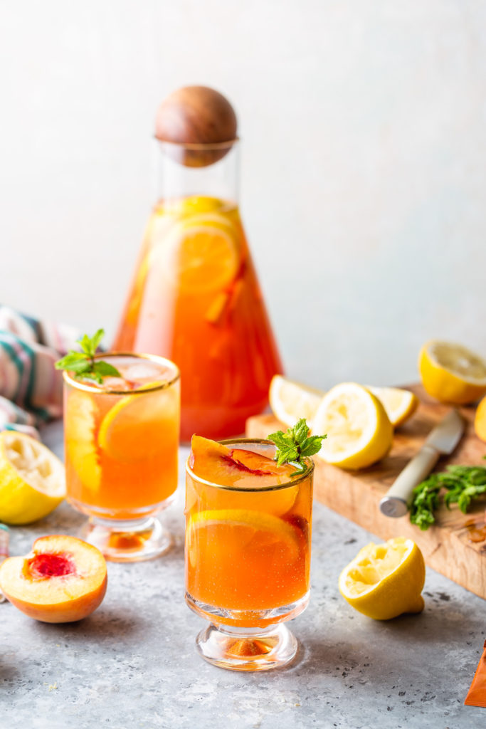 two glasses and a pitcher full of peach iced tea lemonade