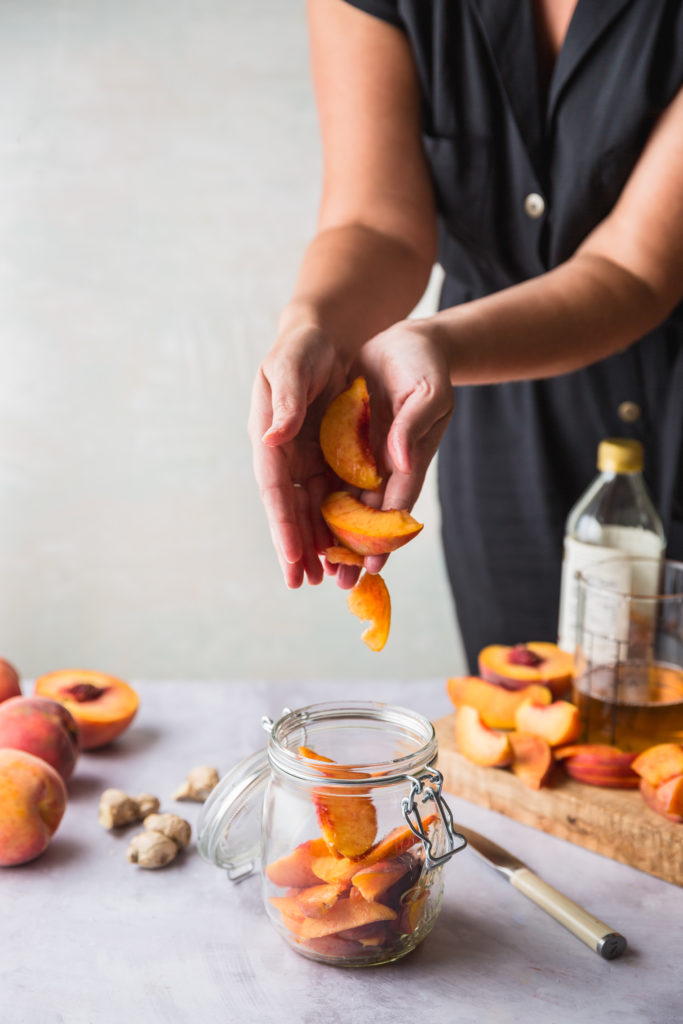 adding fresh peach slices to glass jar to be pickled