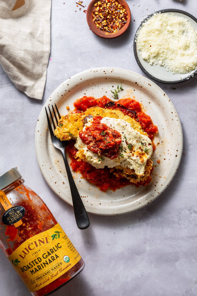 serving of cauliflower parm on white plate next to jar of marinara sauce