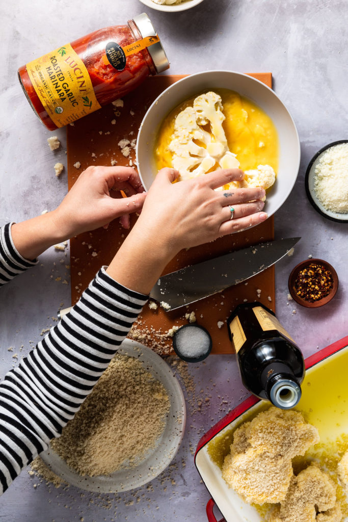 woman dipping cauliflower steak into egg mixture 