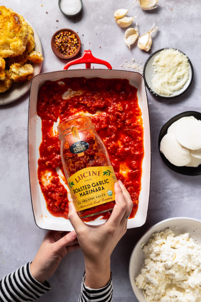 pouring marinara sauce into bottom of baking dish