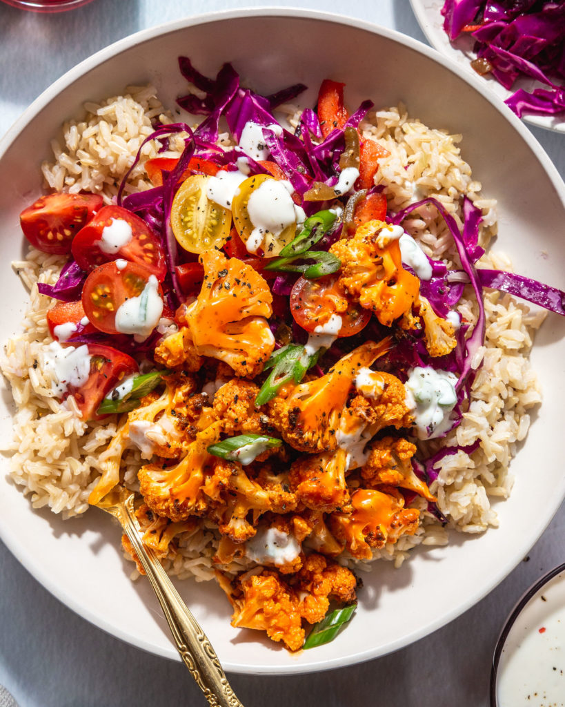 Buffalo Cauliflower Bowl garnished with cherry tomatoes, slaw, and greek yogurt ranch dressing