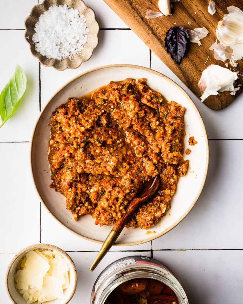 overhead view of Sun Dried Tomato Pesto on white plate with small wood spoon